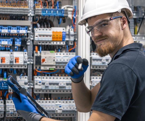 Electrical technician working in a switchboard with fuses, uses a tablet. Happy bearded technician in protective helmet with digital tablet.