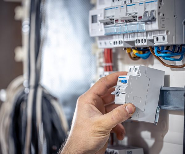 Male electrician at the checkout counter on a blurred background of a switchboard.