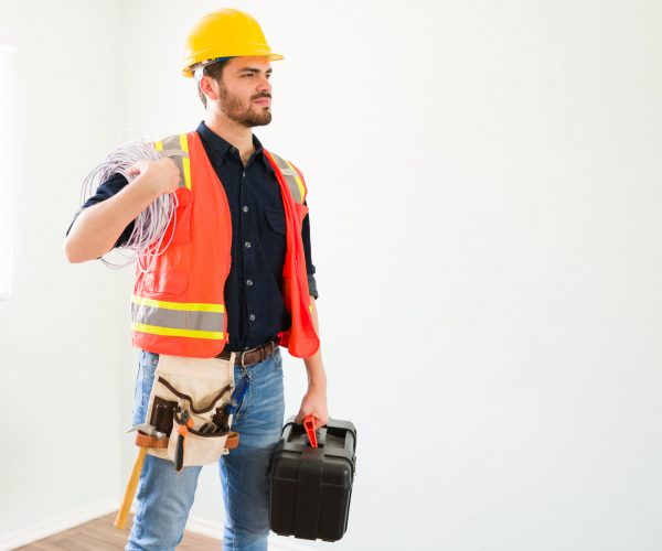 Ready to start my work. Proud attractive electrician with protective gear holding a toolbox and electricity cables